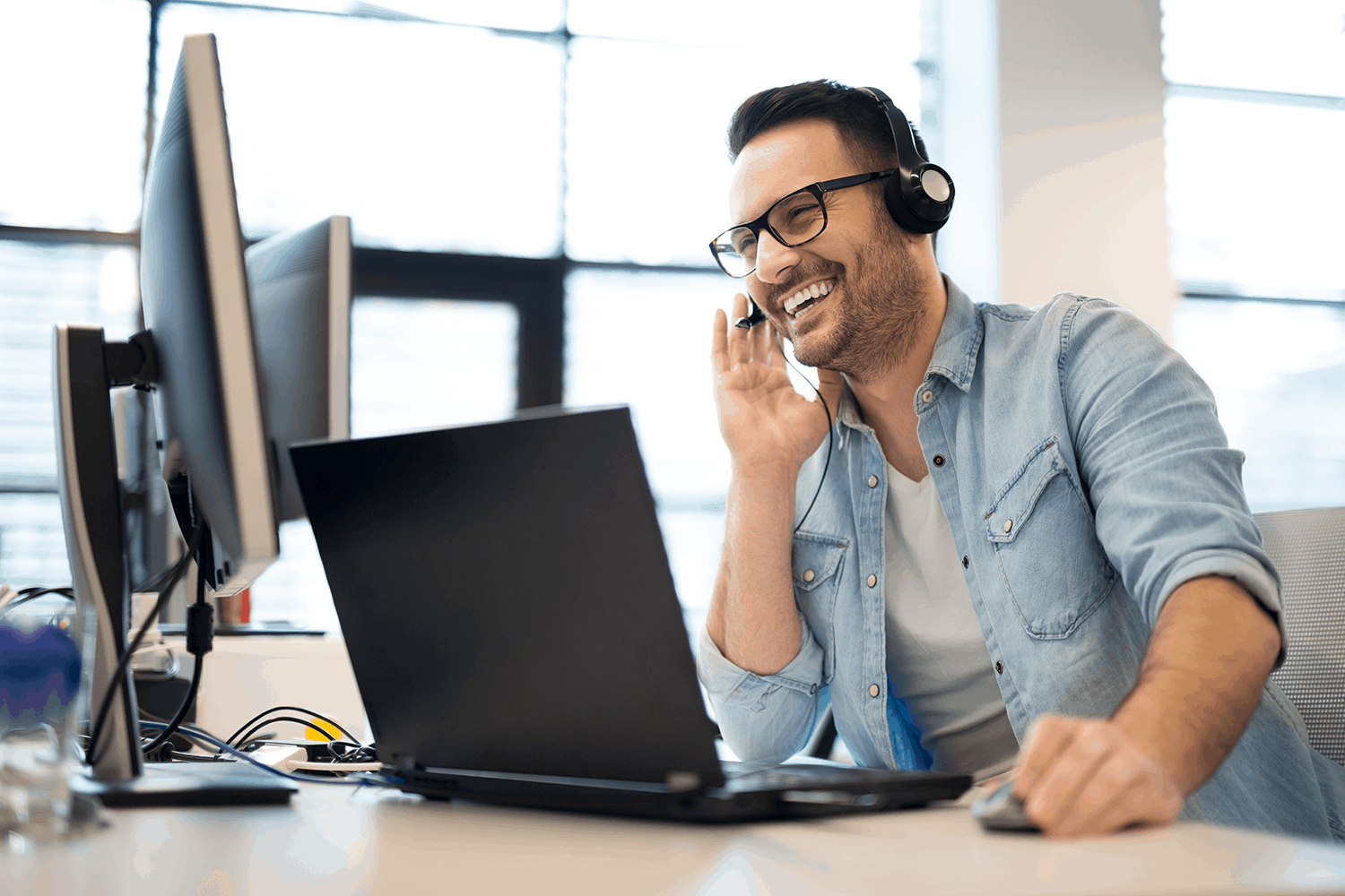 Smiling man working on computer and wearing a headset helping troubleshoot problems and making customers happy
