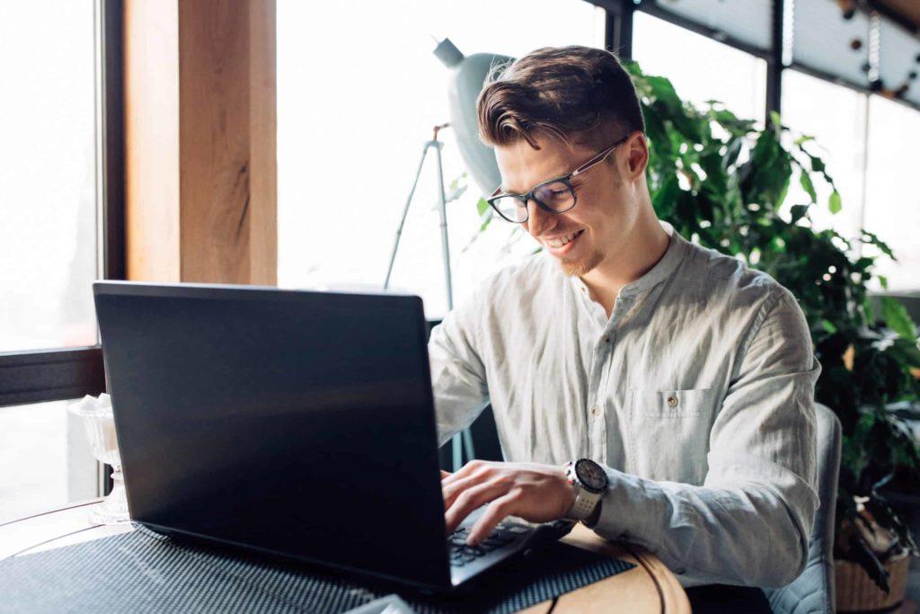 Smiling man wearing glasses and working on IT training on his laptop so he can escape cranky customers in retail and enjoy an IT career