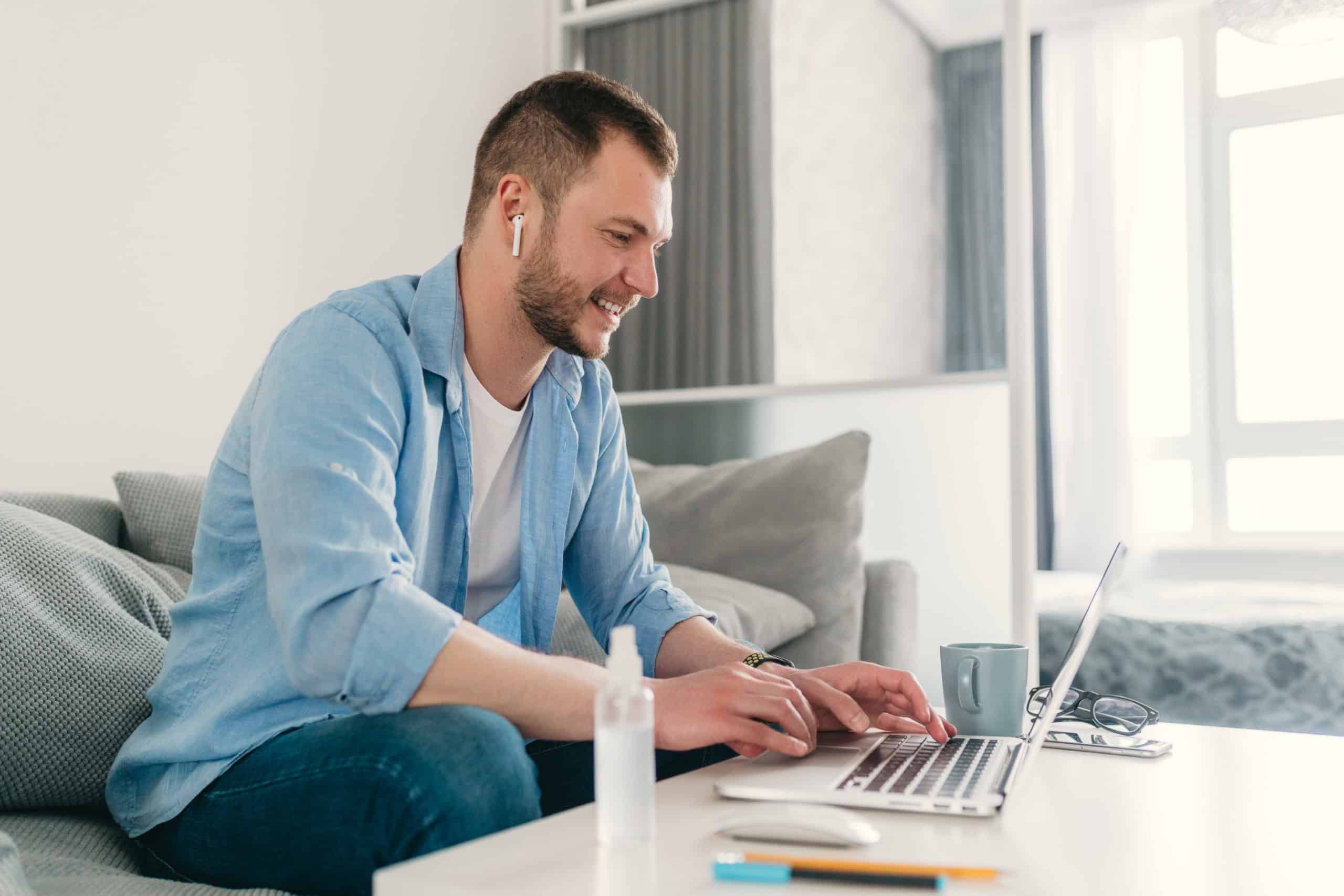 Smiling man with airpods in his ears working on training on his laptop so he can go from hard manual labor jobs to sitting at a desk in an IT career